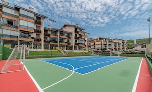 A tennis court with a net, surrounded by multi-story buildings with balconies.