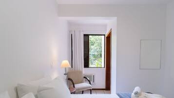 A hotel room with a bed, a chair, a lamp, a window with curtains, and a towel on the bed.