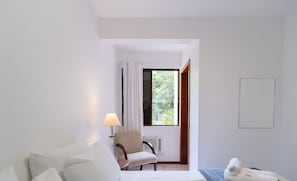 A hotel room with a bed, a chair, a lamp, a window with curtains, and a towel on the bed.