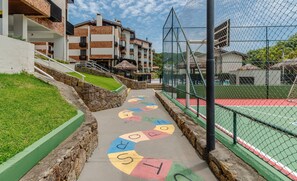 Un chemin bordé de lettres colorées qui mène à un court de tennis, entouré de bâtiments et d’une zone herbeuse.