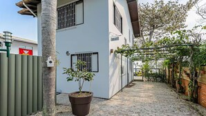 Un camino pavimentado que lleva a un edificio blanco con el número 1647 en la pared, una planta en maceta y una cerca de metal.