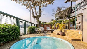 Una piscina rodeada por una terraza de madera, con una zona de estar y plantas en macetas.