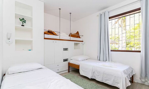 A dormitory room with bunk beds, a wardrobe, a bedside table, and a window with curtains.
