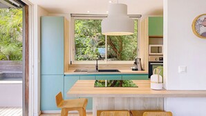 A modern kitchen with a large window, wooden bar stools, and a pendant light.