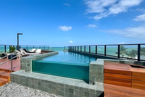 A rooftop infinity pool with a view of the ocean, lounge chairs, and a wooden deck. - Breeze (Joao Pessoa)