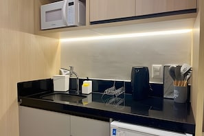 A modern kitchen with a black countertop, a microwave, a coffee maker, and a utensil holder.