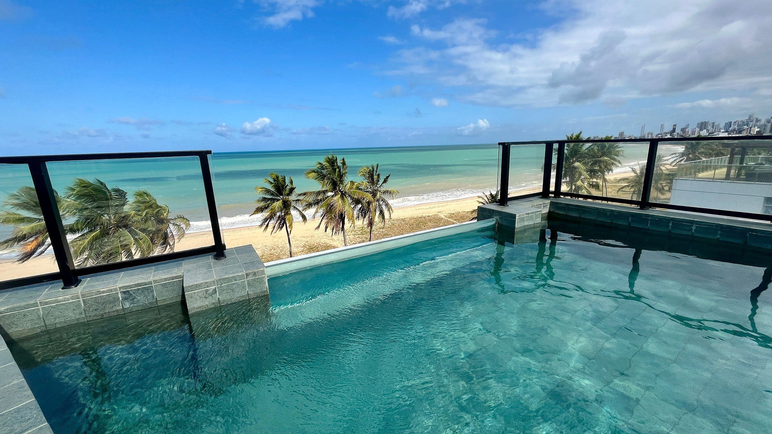A clear view of a swimming pool with a beach and palm trees in the background.