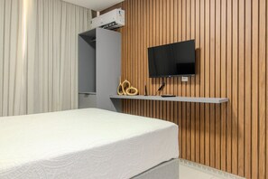 A bedroom with a bed, a mounted TV, and a wooden wall. - Breeze (Joao Pessoa)
