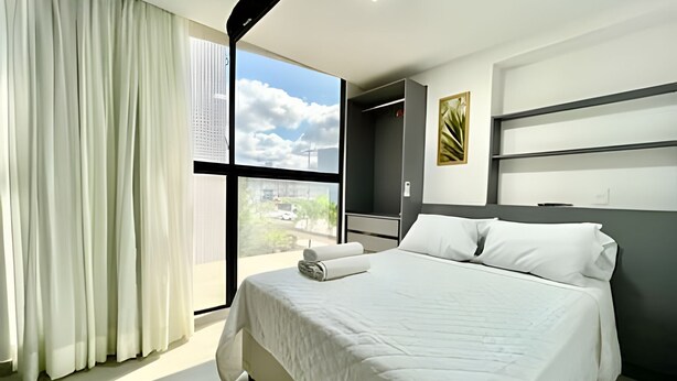 A modern hotel room with a large bed, a view of the city through a large window, and a minimalist design. - Breeze (Joao Pessoa)