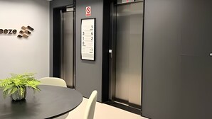 A modern conference room with a black table, white chairs, a potted plant, and two elevators with a no-entry sign above them. - Breeze (Joao Pessoa)