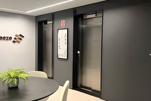 A modern conference room with a black table, white chairs, a potted plant, and two elevators with a no-entry sign above them. - Breeze (Joao Pessoa)