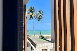 A view from a balcony overlooking a beach with palm trees and a clear blue sky. - Breeze (Joao Pessoa)