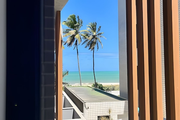 A view from a balcony overlooking a beach with palm trees and a clear blue sky. - Breeze (Joao Pessoa)
