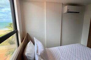 Une chambre d’hôtel avec un lit, une fenêtre donnant sur la plage et un appareil de climatisation.
