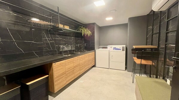 A modern kitchen with black marble countertops, wooden cabinets, a built-in washing machine, and a bar area with stools.