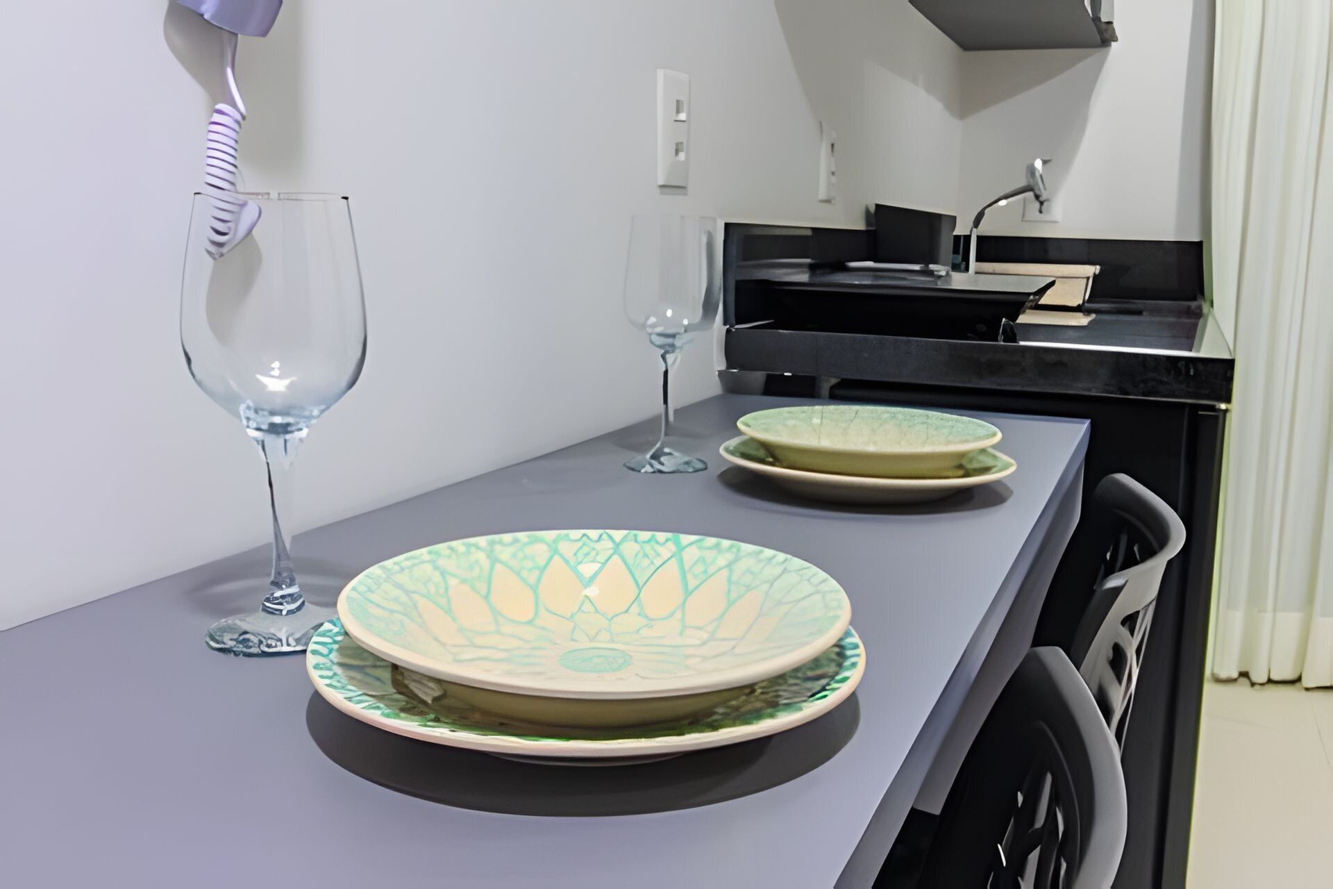 A small kitchenette with a grey countertop, two wine glasses, and a decorative plate.