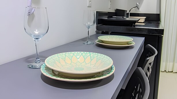 A small kitchenette with a grey countertop, two wine glasses, and a decorative plate. - Breeze (Joao Pessoa)