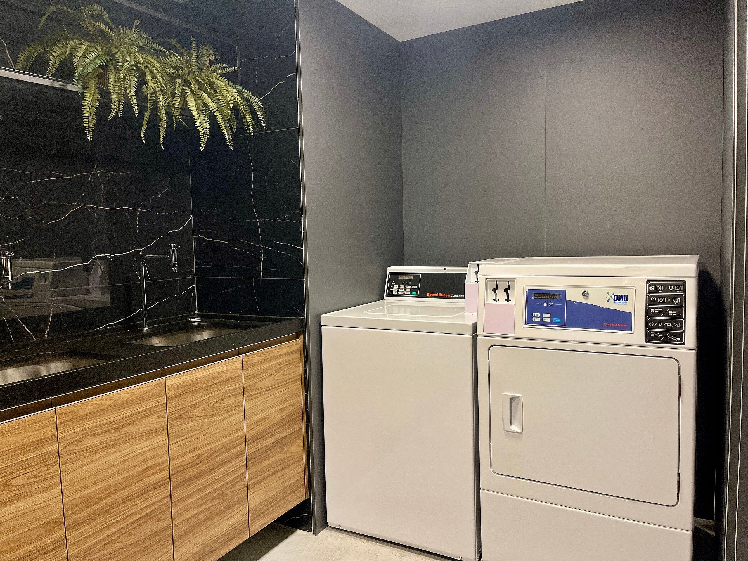 A laundry area with two white washing machines, a black marble backsplash, and wooden cabinets.