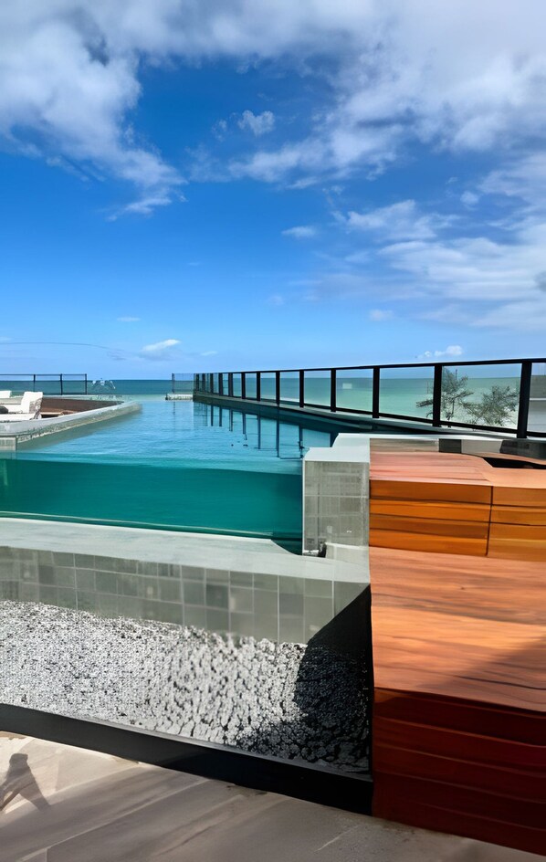 Une piscine séparée du reste par une paroi en verre, une terrasse en bois et une vue sur l’océan.