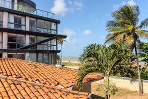 A modern building with a glass facade and a tiled roof, overlooking a beach with palm trees. - Breeze (Joao Pessoa)