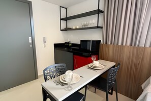 Une cuisine compacte équipée d’un four à micro-ondes, d’un meuble rouge et d’un coin repas avec une table dressée pour deux personnes.