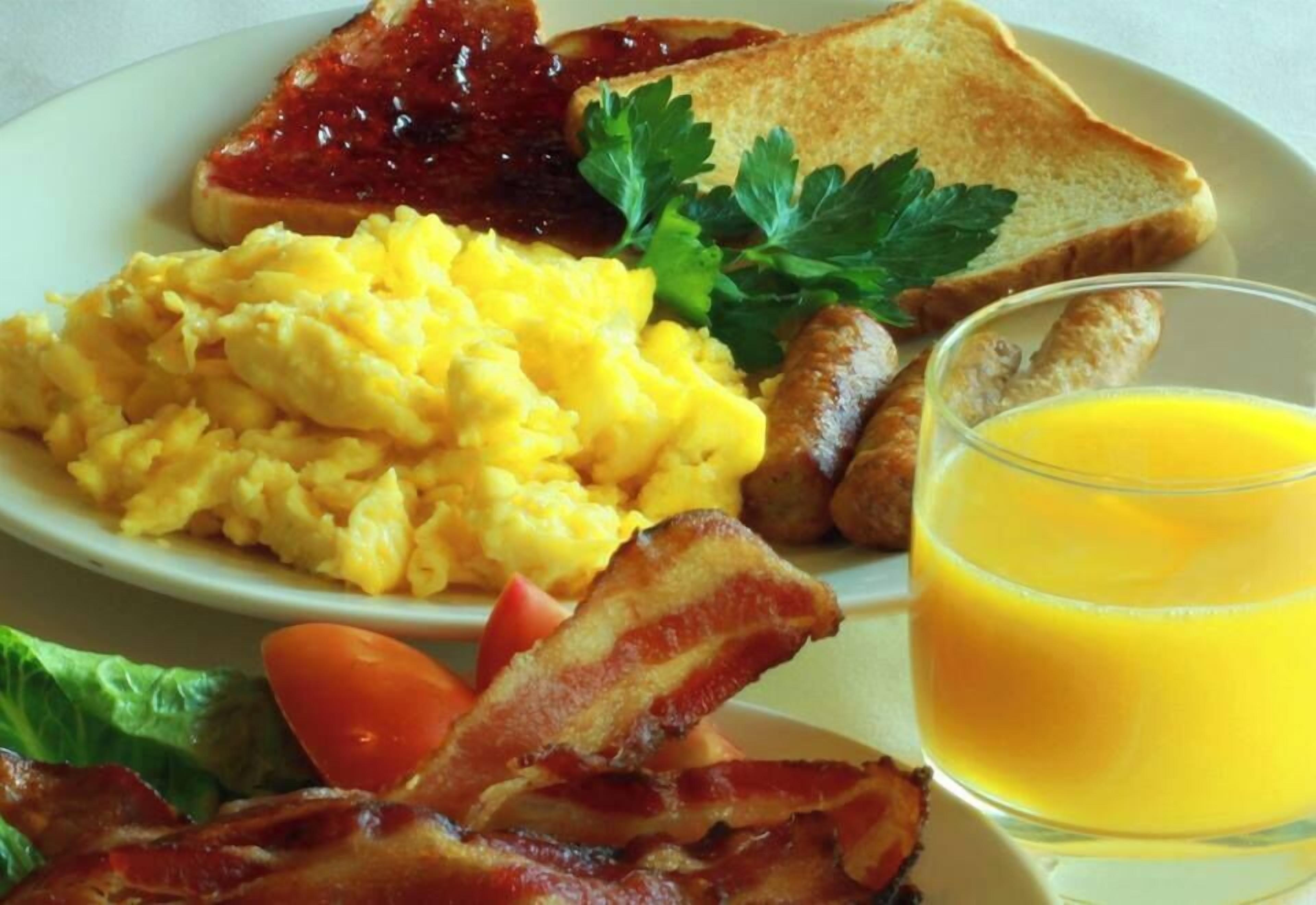A plate with scrambled eggs, bacon, toast, sausage, and a glass of orange juice.