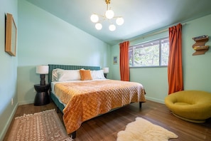 A bedroom with a bed, a nightstand, a chair, a window with curtains, and a ceiling light fixture.