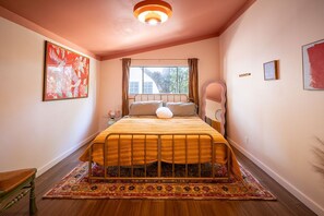 A bedroom with a bed, a window, a rug, and artwork on the walls.