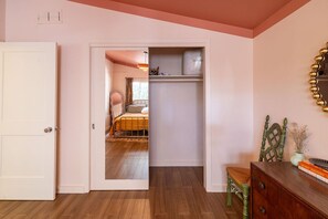 A room with a wooden floor, a white door, a bed with a yellow headboard, a wooden dresser, and a mirror on the wall. - Central Austin Downtown Bungalow (Austin)