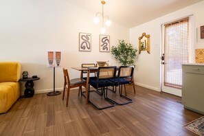 A dining area with a wooden table, four chairs, a floor lamp, and wall art.