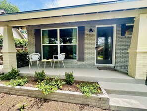 A house with a covered porch, two white chairs, a small table, and a brick exterior.