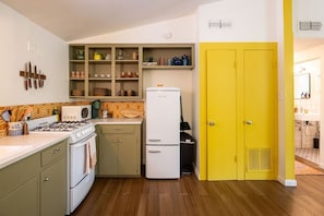 A compact kitchen with a gas stove, microwave, refrigerator, and a yellow door.