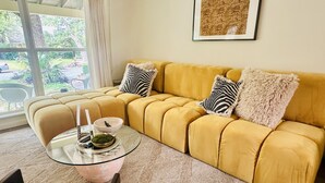 A yellow sofa with zebra-patterned pillows, a glass coffee table with decorative items, and a framed picture on the wall.