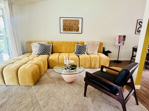 A living room with a yellow sectional sofa, a glass coffee table, and a dark armchair. - Central Austin Downtown Bungalow (Austin)