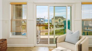 A room with a sliding glass door leading to a balcony with a view of houses and the ocean.
