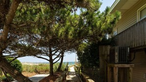 A pathway leading to a beach with a wooden fence and a building with an air conditioning unit.