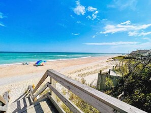 Ein Strand mit einer Holzstege, der zum Ufer führt, einem Strandsonnenschirm und einem klaren, blauen Himmel.