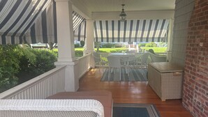 Eine überdachte Veranda mit Korbmöbeln, einer Ziegelwand und Blick auf einen gepflegten Garten.