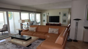 A living room with a large L-shaped brown leather sofa, a coffee table, a TV, and a floor lamp.