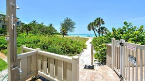 A gated entrance to a beach area with a clear path leading to the ocean, surrounded by lush greenery and palm trees.