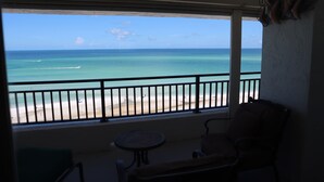 A balcony with a view of the ocean, a table, and a chair.