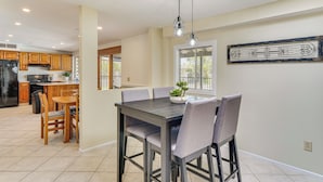 A modern kitchen with wooden cabinets, a black refrigerator, and a dining area with a dark table and grey chairs. - Near Catalina Hiking Trails: Mtn-View Home w/ Pool (Tucson)