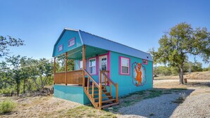 Una casa pequeña de un piso con fachada azul y detalles rosados, que cuenta con una escalera de madera hacia un porche.