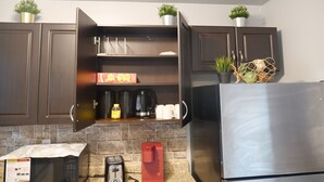 Une cuisine avec des meubles de couleur brun foncé, un réfrigérateur en acier inoxydable, un grille-pain, une machine à café et un four à micro-ondes. Deux plantes en pot sont posées sur les meubles hauts.