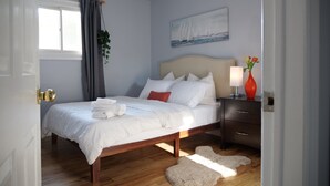 Une chambre à coucher bien rangée, avec un lit, une table de chevet et un tableau accroché au mur.