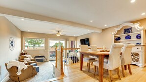 Un salon spacieux avec une table à manger en bois, des sièges confortables, un escalier et une vue sur l’extérieur.