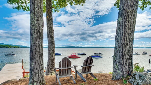 Une vue sur le lac, avec deux fauteuils Adirondack placés face à un quai et à des bateaux sur l’eau.