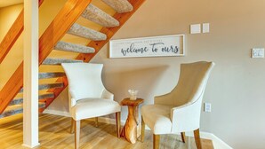 Un intérieur moderne avec un escalier en bois, deux fauteuils rembourrés, une petite table en bois et un panneau décoratif mural.