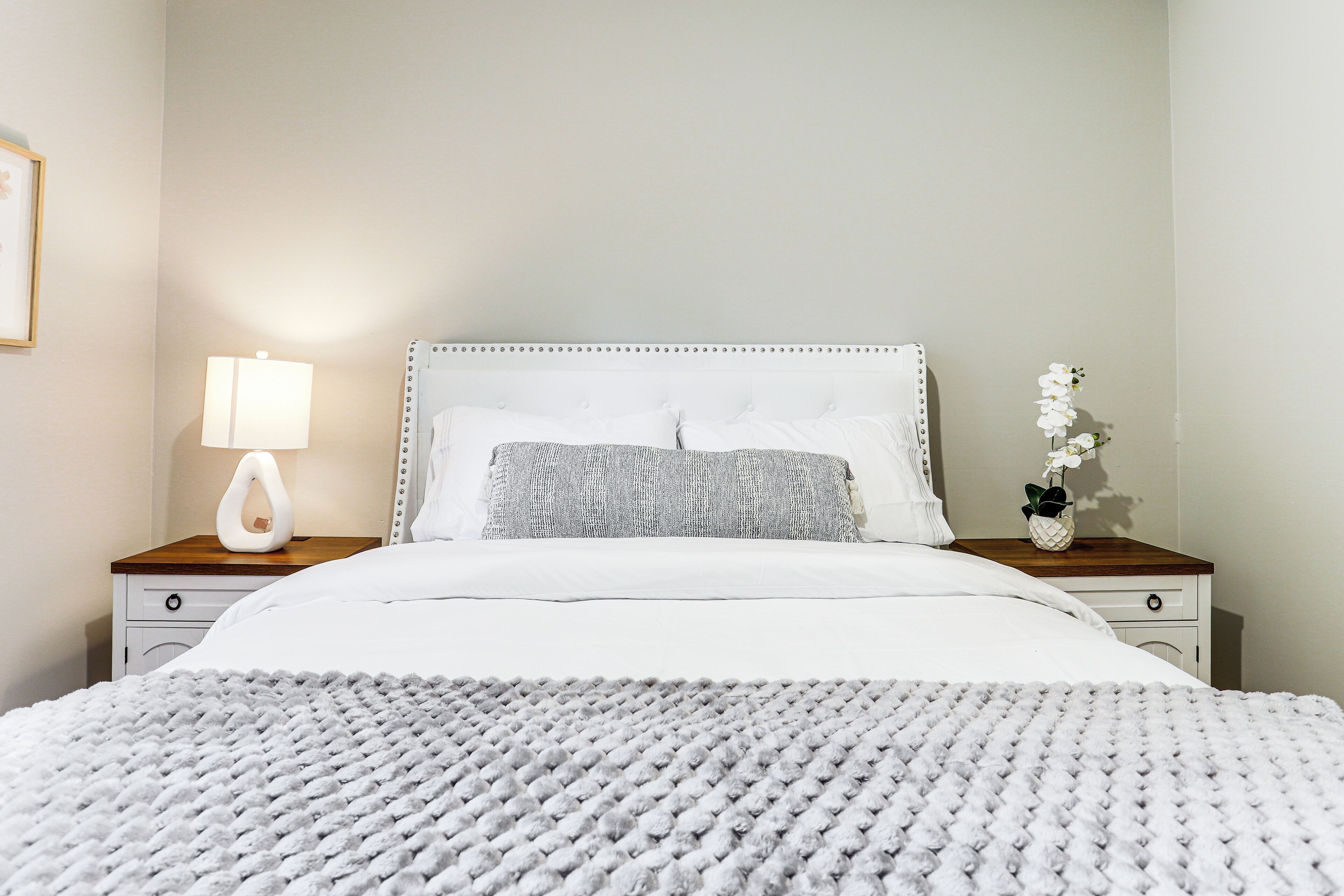Un letto rifatto con copriletto bianco e una coperta a maglia grigia.