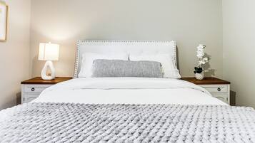 Un letto rifatto con copriletto bianco e una coperta a maglia grigia.